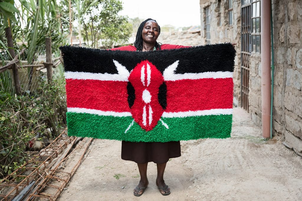 A Kenyan woman smiles while holding Kenya's flag in front of her.