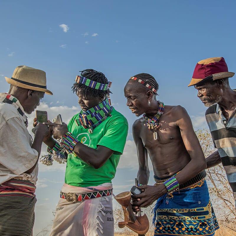 Kitabo Wele, 25, Afriscout promoter, discusses about the use of Afriscout application with a pastorialists Muda Gela, 66,  Andulsha Kefa, 45 and Kole Kilkila, 53 (right to left) in Hamer Woreda, South Omo zone, SNNPR, Ethiopia.