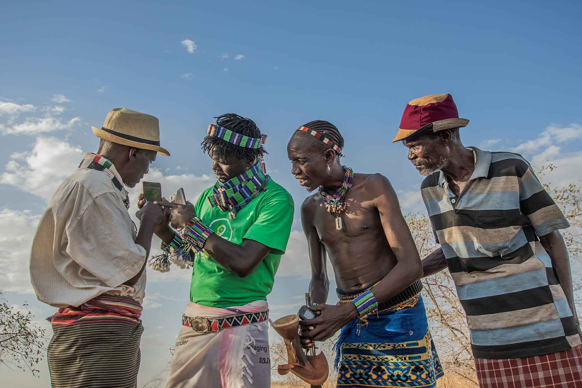 Kitabo Wele, 25, Afriscout promoter, discusses about the use of Afriscout application with a pastorialists Muda Gela, 66,  Andulsha Kefa, 45 and Kole Kilkila, 53 (right to left) in Hamer Woreda, South Omo zone, SNNPR, Ethiopia.
